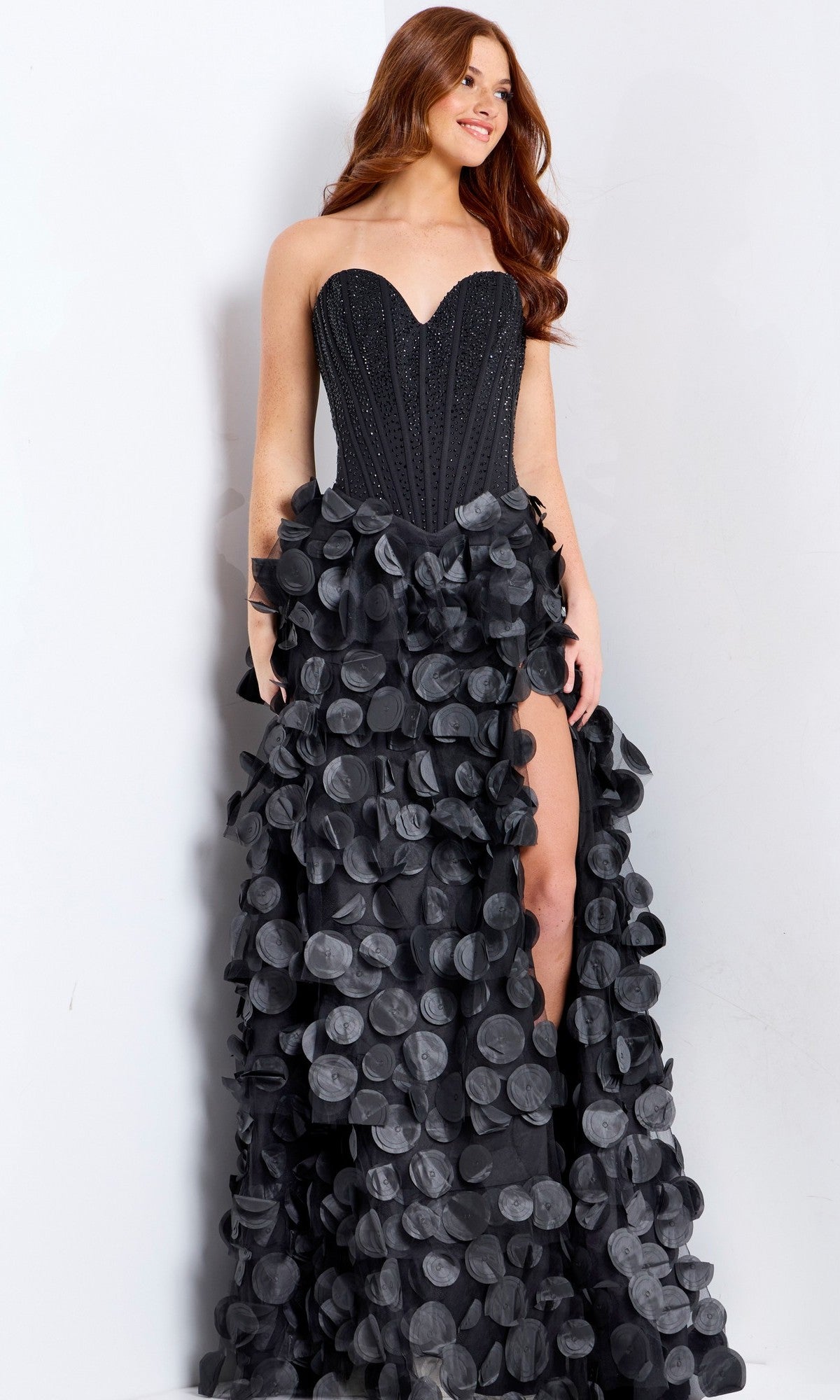 Woman wearing the Long Prom Dress: Jovani 49384 with a strapless beaded corset bodice and voluminous 3D petal A-line skirt with large circular ruffles, posing against a white background.